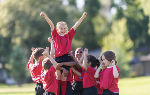 a group of kids outdoors in uniforms holding up a girl in celebration